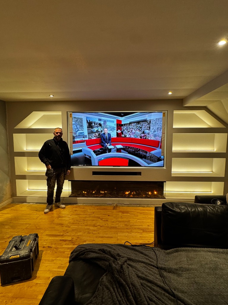 Bespoke media wall installation featuring integrated shelving, warm LED lighting, and a panoramic electric fireplace