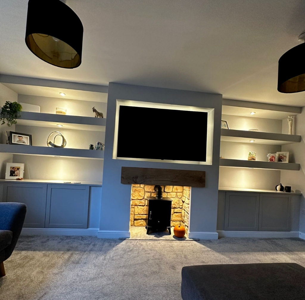 Grey media wall design featuring a recessed TV and traditional wood-burning stove with natural stone surround